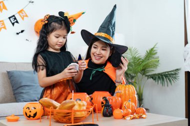 Cadılar Bayramı kostümü giymiş bir anne ve kız evde balkabağı ve süslemelerle kutlama yapıyorlar..