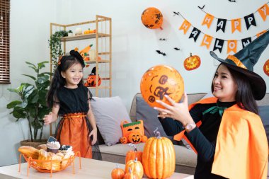 Neşeli bir anne ve kız evde Cadılar Bayramı şenliklerinin keyfini çıkarıyor. Etrafı şenlikli dekorasyonlarla çevrili ve temalı kostümler giyiyor..