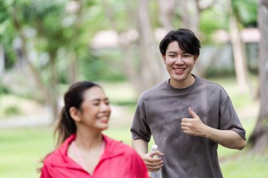 Genç bir çift parkta koşuyor, gülümsüyor ve su şişeleriyle susuz kalıyorlar, sağlıklı ve aktif bir yaşam tarzını destekliyorlar..