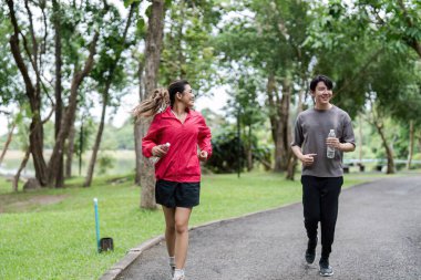 Genç bir çift yemyeşil bir parkta birlikte koşuyor, fitness, sağlık ve aktif bir yaşam tarzını destekliyor..