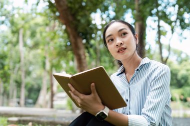 Dışarıda dizüstü bilgisayar ve defterle çalışan genç bir dijital göçebe, parkta esnek ve modern bir çalışma tarzını benimsiyor..