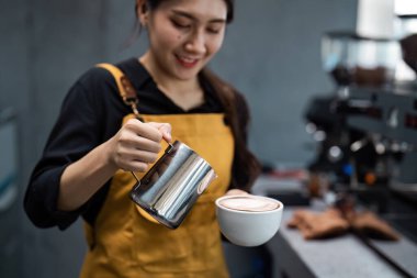 Sarı önlüklü yetenekli bir barista modern bir kahve dükkanında latte sanatı yaratıyor, profesyonel bir espresso makinesiyle kahve yapma sanatını sergiliyor..