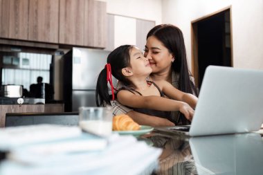 Modern bir mutfak ortamında kızıyla kaliteli zaman geçirirken evde laptopuyla çalışan bir anne..