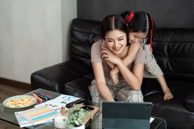 Bir anne ve kızı evde çalışırken birbirlerine bağlanıyorlar, rahat bir kanepede tablet kullanıyorlar, renkli kırtasiye ve atıştırmalıklarla çevrili..