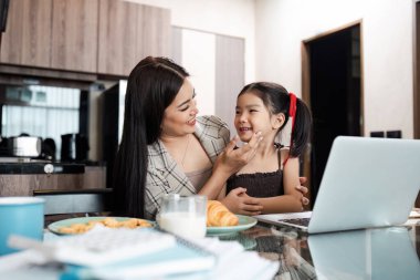 Modern bir mutfak ortamında kızıyla kaliteli zaman geçirirken evde dizüstü bilgisayarla çalışan bir anne..