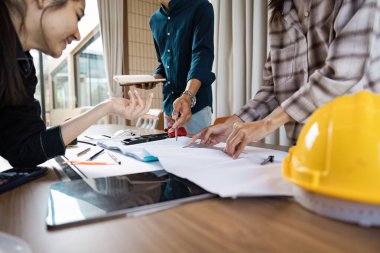 Güvenlik kaskı ve aletleri olan modern bir ofis ortamında plan ve inşaat planlarını tartışan bir grup mimar..