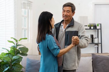 Yaşlı bir çift, doğal ışık ve iç mekan bitkileriyle dolu oturma odalarında dans ederek hassas bir anı paylaşıyor..