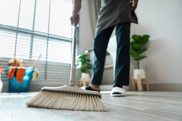 A person cleaning the floor with a broom in a bright, modern home interior featuring houseplants and natural light.