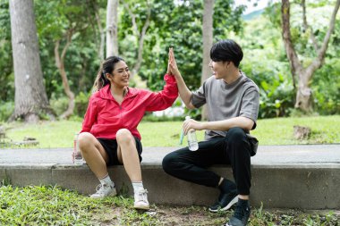 Parkta egzersiz yapmaya ara veren genç bir çift su şişelerini tutarken birbirlerine gülümseyip beşlik çakıyor..