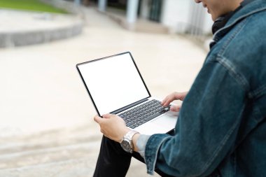 Kot ceketli genç bir adam dışarıda boş ekranı olan dizüstü bilgisayar kullanarak kopya alanı sağlıyor. Şehir arkaplanı.