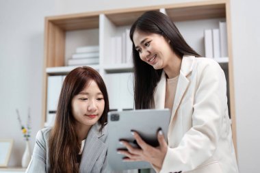 Çağdaş ofis ortamında bir tablette birlikte çalışan iki iş kadını takım çalışması ve iş dünyasındaki teknolojiyi sergiliyorlar..