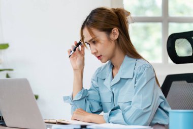 Evde çalışan genç bir kadın, bilgisayarına odaklanmış modern bir ofis ortamında doğal ışıkla.