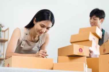 Genç Asyalı bir kadın meşgul ofisinde siparişleri hazırlıyor ve çevrimiçi dükkanı için sorunsuz bir teslimat sağlıyor..