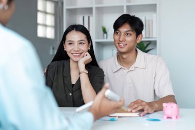 Masadaki pembe kumbarayla sembolize edilen tasarruf planları hakkında bir finans danışmanıyla görüşen genç bir çift..