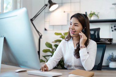 Gülümseyen çağrı merkezi ajanı, kulaklık takıyor, modern ofis ortamında bir masada çalışıyor, müşteri hizmetleri sunuyor..