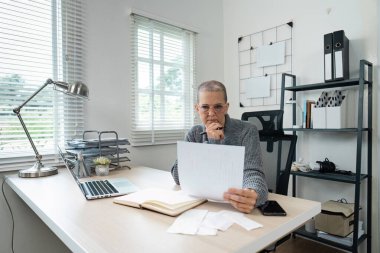 Emeklilik için tasarruf ve bütçe planlamasına odaklanan, ev ofisindeki mali belgeleri inceleyen yaşlı bir kadın..