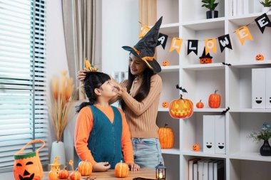 Evde Cadılar Bayramı şenliklerinin tadını çıkaran, kostüm giymiş ve etrafı şenlikli süslemelerle çevrili bir anne ve kız..