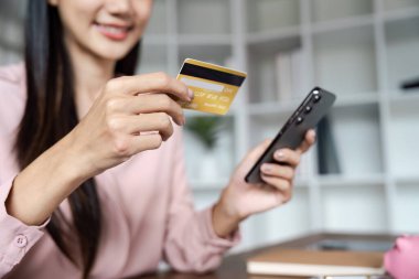 Bir kadın kredi kartıyla ödeme yapmak için telefonunu kullanıyor. Gülümsüyor ve alışveriş yaptığı için mutlu.