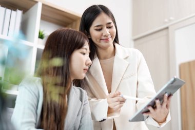 Çağdaş ofis ortamında bir tablet üzerinde çalışan iki iş kadını, takım çalışması ve işbirliği sergiliyor.