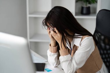 Ofis sendromu belirtileri gösteren genç profesyonel bir kadın. Masasında bilgisayar ve belgelerle kendini yorgun ve stresli hissediyor..