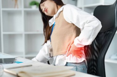 Modern bir ofiste çalışan genç bir kadın masasında çalışırken ciddi sırt ağrısı çekiyor ve işyerindeki rahatsızlığı vurguluyor..