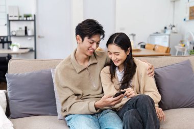 Keyifli bir çift kanepede oturuyor, birbirleriyle eğlenirken rahat, modern bir oturma odasında akıllı bir telefona bakıyorlar..