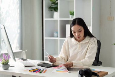 Modern bir ofiste dijital tablet ve renk örnekleri kullanarak yaratıcı bir proje üzerinde çalışan genç bir bayan tasarımcı..