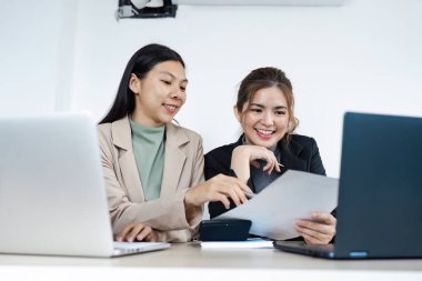 İki iş kadını bir proje üzerinde birlikte çalışıyor, belgeleri tartışıyor ve çağdaş ofis ortamında dizüstü bilgisayar kullanıyorlar..