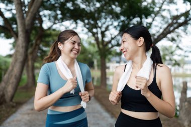 İki kadın parkta koşuyor, gülümsüyor ve sohbet ediyorlar, boyunlarında havlularla, sağlıklı bir sabah egzersizi yapıyorlar..