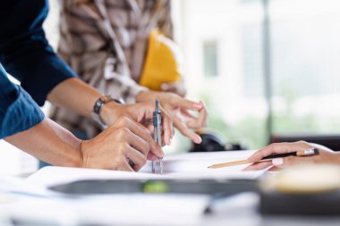 Modern bir ofis ortamında teknik çizimler ve araçlar kullanarak proje planları üzerinde birlikte çalışan mühendislerin yakın çekimleri.