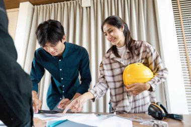 İki genç mühendis bir projede birlikte çalışıyorlar, planları gözden geçiriyorlar ve modern ofis ortamında güvenlik donanımı giyiyorlar..