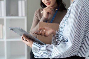 Modern ofis ortamında dijital tablet ve pano kullanarak çalışmayı tartışan iki iş adamı..