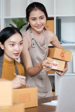 Çevrimiçi işlerinde çalışan iki genç kadın, modern bir ofis ortamında karton kutular hazırlıyorlar..