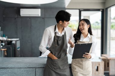 Önlüklü iki genç girişimci modern bir küçük işletme kafe ortamında iş stratejisini tartışıyor, takım çalışması ve işbirliği sergiliyor..