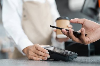 Müşteri, modern dijital ödeme yöntemlerini vurgulamak için bir kahve dükkanında akıllı telefon kullanarak ulaşılmaz bir ödeme yapar..