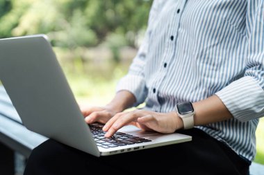 Açık hava parkında dizüstü bilgisayarda çalışan, çizgili gömlek giyen, zeki bir adam üretkenliğe ve modern teknolojiye odaklanıyor..