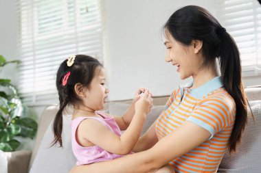 Güneşli bir oturma odasında, koltukta oturmuş gülümseyen neşeli bir anne ve kız..