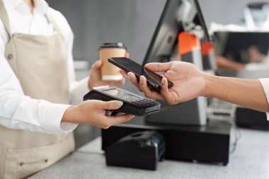 Müşteri, elinde kahve barında elinde kahve barmeniyle akıllı bir telefonla telefon görüşmesi yapıyor..