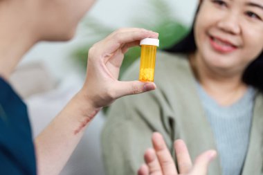 Bir sağlık uzmanı tıbbi konsültasyon sırasında gülümseyen bir hastayla ilaç tartışırken reçeteli bir şişe tutar..