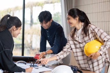 Bir grup mimar bir proje üzerinde birlikte çalışıyor, planları tartışıyor ve çağdaş ofis ortamında inşaat araçları bulunduruyorlar..