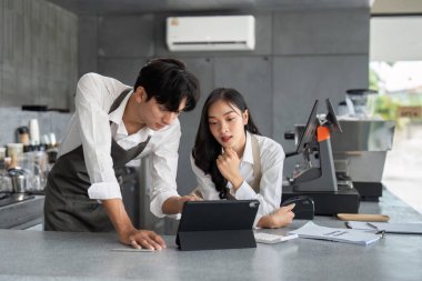 Çağdaş bir kahve dükkanında birlikte çalışan iki genç barmen, sipariş ve işleri yönetmek için dijital tablet kullanıyorlar..