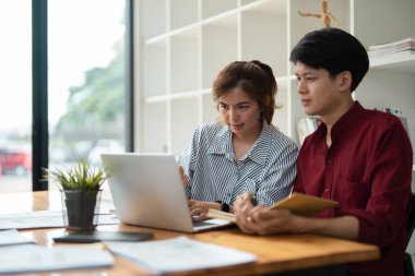 Modern bir ofiste dizüstü bilgisayarda birlikte çalışan iki genç profesyonel doğal ışık ve rahat bir atmosferi var..