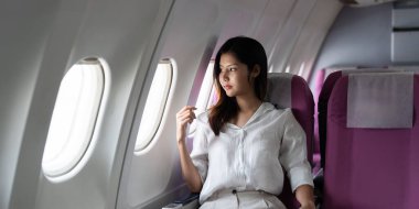 Gündelik giysiler içinde genç bir kadın uçak penceresinin yanında oturur ve uçuş sırasında dışarıya bakar. Kabinin içi modern ve rahattır..