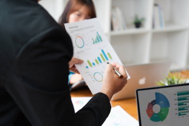 Çağdaş bir ofis ortamında düzenlenen bir iş toplantısında finansal veri ve grafikleri tartışan profesyoneller.