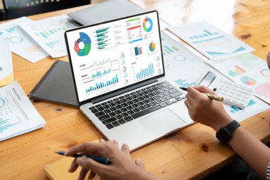 İş dünyası ekibi, ofis toplantısı sırasında elinde grafikler ve çizelgeler olan bir dizüstü bilgisayardaki mali verileri analiz ediyor. Ortak çalışma ortamı.