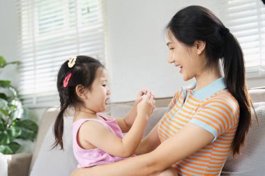 Güneşli bir oturma odasında, koltukta oturmuş gülümseyen neşeli bir anne ve kız..
