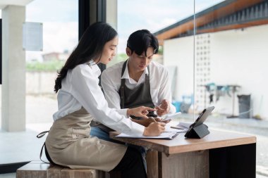 Önlüklü iki genç barmen dijital tablet ve modern bir kahve dükkanında doküman kullanarak bir iş planı üzerinde birlikte çalışıyorlar..
