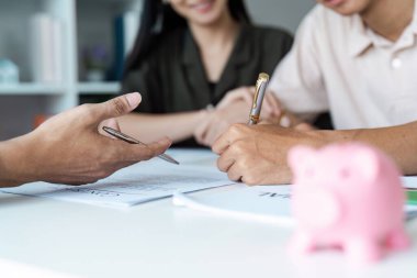 Mali danışmanlarla tasarruf planlama, evrakları imzalama ve ön planda bir domuz kumbarası..