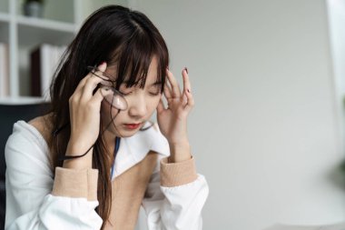 Modern bir iş ortamında, ofis sendromu belirtileri gösteren stres ve baş ağrısı yaşayan genç bir ofis çalışanı..