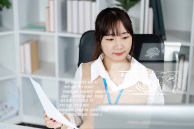 Modern ofis ortamında verileri fütüristik holografik arayüzlerle analiz eden, bilgisayar üzerinde çalışan genç profesyonel bir kadın..